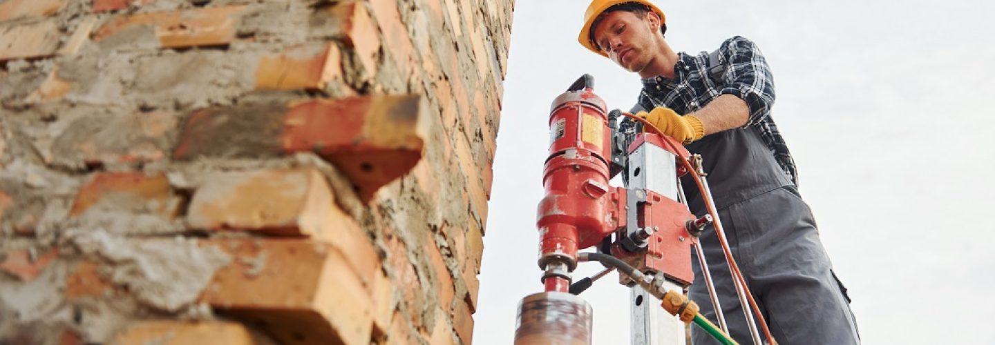 Uses blending drill. Construction worker in uniform and safety equipment have job on building.